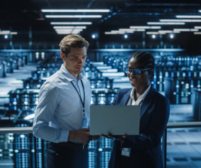 Data Center Female System Administrator and Male IT Specialist talk, Use Laptop. Information Technology Engineers work on Cyber Security Network Protection in Cloud Computing Server Farm.